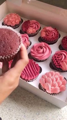 a person holding a cupcake in front of a box of pink frosted cupcakes