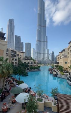 the city is surrounded by tall buildings and blue water, with people sitting at tables in front of them