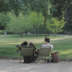 two people sitting on lawn chairs in a park with one person holding the other's head