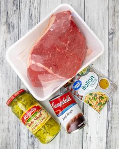 raw meat in a white bowl next to canned vegetables and seasonings on a wooden table