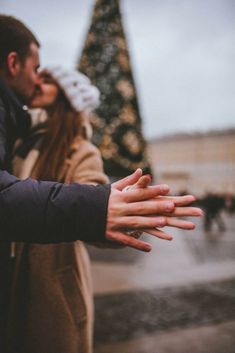 a man and woman standing next to each other near a christmas tree with their hands out