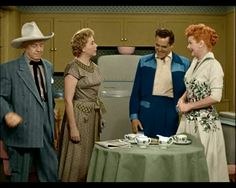 three people standing around a table with cups and saucers on it in front of a refrigerator