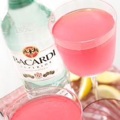 a glass filled with pink liquid next to a bottle of bacardi water and lemon wedges