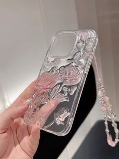 a hand holding a clear phone case with flowers and beads hanging from the back, in front of a mirror