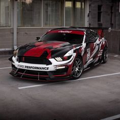 a red and black mustang car parked in a parking lot next to a building with windows