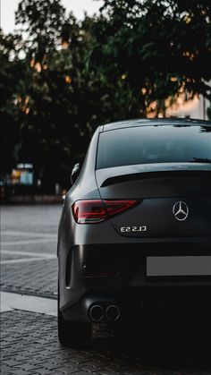 the back end of a black mercedes cls parked in front of a tree lined street