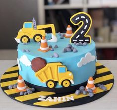 a blue and yellow birthday cake with construction vehicles on it's side, the number two is for 2