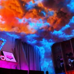 a man standing at a podium in front of a colorful cloud filled sky above him