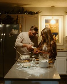 a man and woman standing in a kitchen preparing food on top of a counter next to a refrigerator