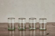 four glasses sitting on top of a wooden table next to each other and one is empty