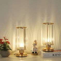 two glass lamps sitting on top of a table next to a book and potted plant