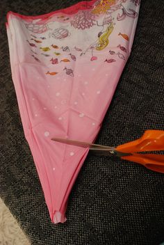 an orange pair of scissors next to a pink umbrella