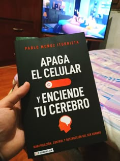 a person holding up a book in front of a tv set with the words apaga el celuar y encende de tu cerebro written on it