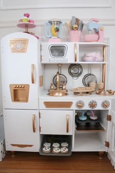 a white toy kitchen with wooden floors and shelves