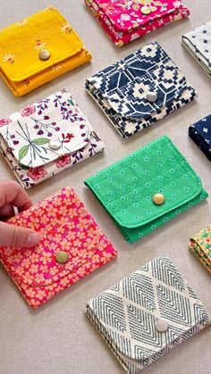 a hand is pointing at several small wallets on the table, all different colors and patterns