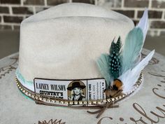 The Lainey Wilson Concert Wide Brimmed Cowgirl Hat is perfect for attending that upcoming Lainey concert... Or just displaying your fan crush!   Colors: Cream Sand (Light Tan) Cognac (Dark Tan) Each hat displays a ticket stub for the Lainey Wilson's Country's Cool Again Tour and a floral arrangement burned-by-hand around the hat brim.  Flowers are just my creative arrangements, but feel free to let me know if you have a specific flower that you would like me to include.  I've had requests for magnolias, roses, and sunflowers just to name a few. If you would like a personalized name, phrase, or song lyric around the brim, just include in the messaging with your order and I'll be happy to include for you. The standard banding and feathers come in neutrals and turquoise, but I'll be happy to Custom Handmade Fedora For Country Events, Handmade Country Style Hat Bands For Kentucky Derby, Handmade Hat Bands For Kentucky Derby, Lainey Wilson Concert, Hat Customization, Hat Burning, Hat Bar, Lainey Wilson, Hand Burn