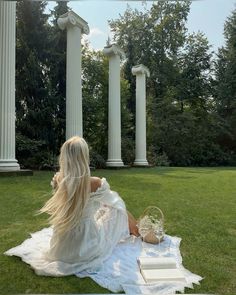 a woman sitting on top of a white blanket in the grass next to two pillars