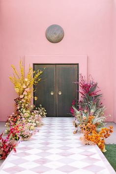 a table with flowers on it in front of a pink wall and two doors that lead into the room