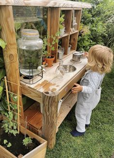 a little boy standing next to a wooden planter filled with plants and water in it