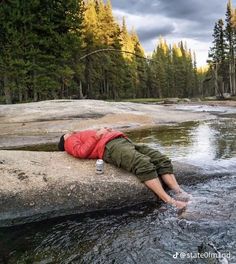 a man laying on top of a rock next to a river