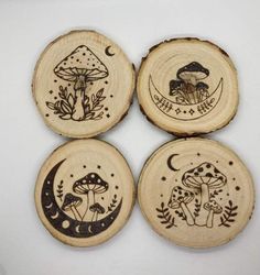 four wooden coasters with designs on them sitting on a white surface, one has mushrooms and the other is a mushroom