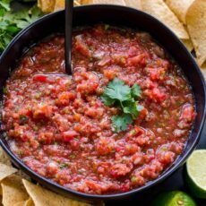 a black bowl filled with salsa surrounded by tortilla chips and cilantro