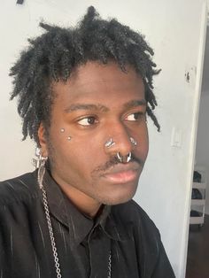 a man with piercings on his nose wearing a black shirt and silver chain around his neck