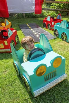 a little boy riding in a toy car on the grass with other toys behind him