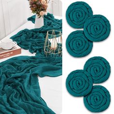 four teal towels on a bed next to a vase with flowers and a candle