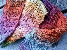 three knitted scarves sitting on top of a wooden bench