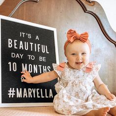 a baby sitting next to a sign that says it's a beautiful day to be 10 months