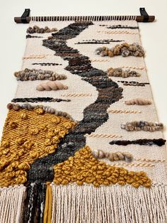 a close up of a weaving on a white surface with black and yellow threads hanging from it's sides