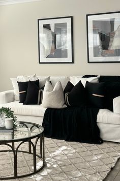 a living room with white couches and black pillows on the sofa, two framed pictures above them