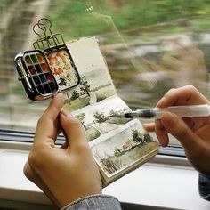 a person holding an open book and pen in their hand while looking out the window