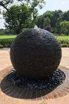 a large metal ball sitting on top of a stone walkway next to a lush green park