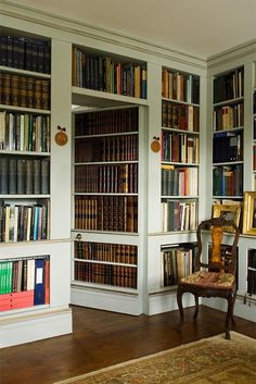 a room filled with lots of books on top of white bookcases next to a wooden chair