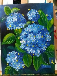 a painting of blue flowers is shown on a easel next to some paintbrushes