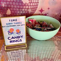 a bowl of candy sits next to a sign that says i like shiny things but i'd marry you with candy rings