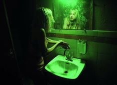 a woman standing in front of a bathroom mirror with green light shining on her face