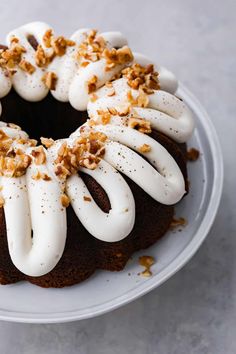 a chocolate bundt cake with white frosting and walnuts on top, sitting on a plate