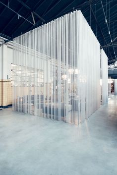 an empty room with sheer curtains covering the walls and tables in front of it on concrete flooring