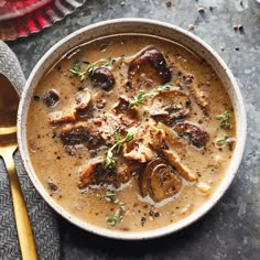 a bowl filled with meat and mushrooms next to a spoon on top of a table