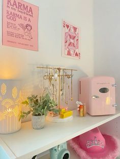 a white shelf topped with lots of items next to a pink refrigerator and potted plant