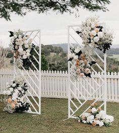 an outdoor ceremony setup with flowers and greenery on the grass near a white picket fence