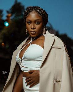 a woman in a white top and tan coat posing for a photo with her hands on her hips