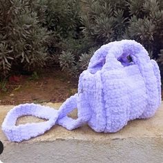 a purple handbag sitting on top of a cement slab next to bushes and shrubbery