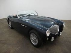 an old black sports car is parked in a room with a white wall behind it