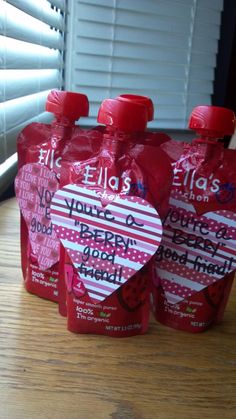 three red heart shaped candy bags sitting on top of a wooden table next to a window