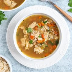 two bowls of chicken and rice soup on a blue surface with spoons next to it