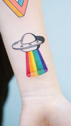 a small tattoo on the wrist of a person with a rainbow and an alien spaceship